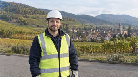 Personne fictive équipée devant des vignobles et des maisons à colombages, dans un cadre inspiré de la région Grand Est
